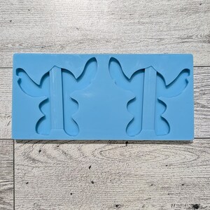 May include: A light blue silicone mould featuring two stylized antler shapes. The mould is rectangular and sits on a light wood-grain surface. The antler shapes have a central stem and curved, branching tips.