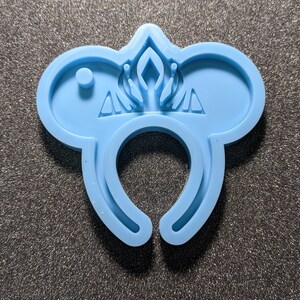 May include: Light blue silicone mold for making a pair of mouse ears with a crown design. The mold has a hole in the center for a headband.