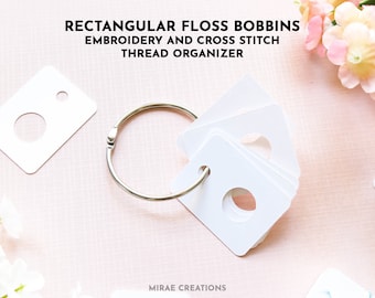 May include: White rectangular floss bobbins with a round hole in the center, organized on a silver ring. The bobbins are designed for embroidery and cross stitch thread organization. The text "RECTANGULAR FLOSS BOBBINS EMBROIDERY AND CROSS STITCH THREAD ORGANIZER" is at the top of the image.