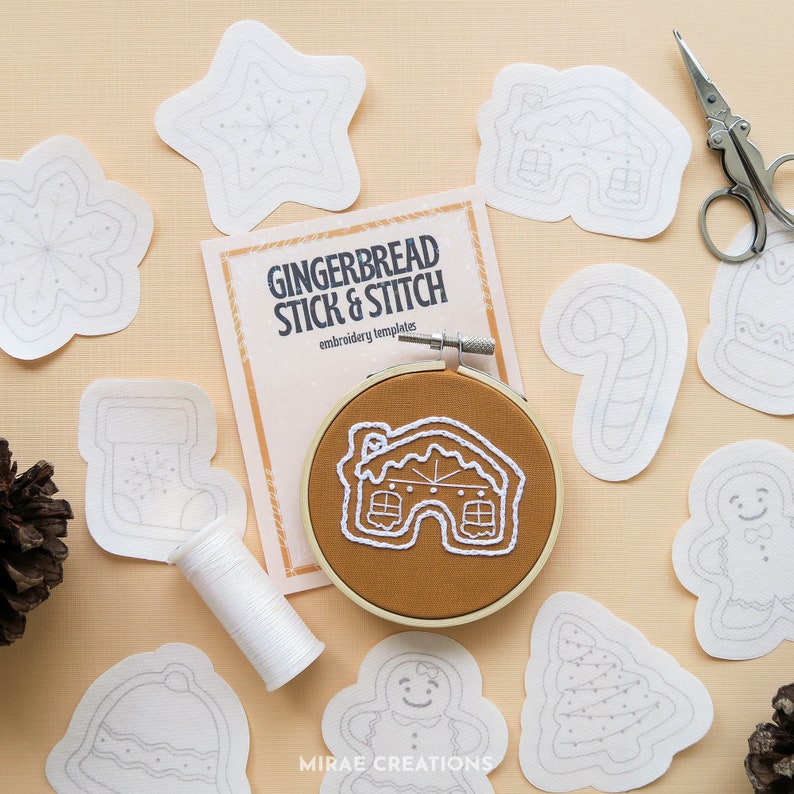 May include: A set of 10 gingerbread cookie embroidery templates, including a star, a house, a stocking, a candy cane, a gingerbread person, a tree, and a bell. The templates are printed on white paper and are ready to be stitched. The text "Gingerbread Stick & Stitch" is printed on a brown card.
