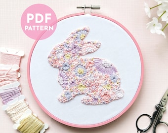 May include: A PDF pattern for a floral bunny embroidery project. The pattern is displayed in a pink embroidery hoop with a white background. The bunny is made up of pink, purple, and yellow flowers.