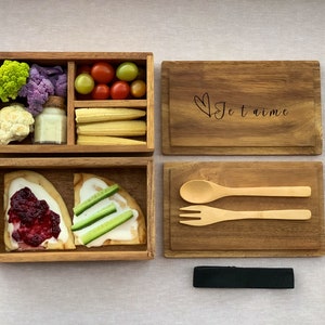 K&ouml;nnte beinhalten: Eine Lunchbox aus Holz mit zwei F&auml;chern. Das obere Fach enth&auml;lt Blumenkohl, Brokkoli, Mais, Tomaten und ein kleines Glas Dip. Das untere Fach enth&auml;lt zwei St&uuml;cke Fladenbrot mit Belag. Die Lunchbox wird mit einem Tablett aus Holz mit L&ouml;ffel und Gabel, einer Holzkiste mit der Gravur "Je t'aime" und einem schwarzen Band geliefert.