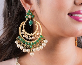 May include: Gold-toned chandelier earrings with a crescent moon design. The earrings feature green teardrop-shaped stones, small white pearls, and a large white pearl at the bottom. The earrings are a statement piece of jewelry.