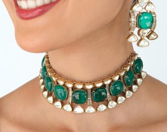 May include: A gold-toned choker necklace and matching drop earring set featuring large, smooth, oval-shaped green cabochon stones. The jewelry is accented with small, clear, triangular-cut stones set in a metallic frame with a textured finish.