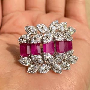 Peut inclure: Bague argentée ornée de pierres précieuses rectangulaires rose foncé, entourées de pierres d'accent claires et scintillantes. Le design intègre des formes de feuilles, créant une esthétique florale ou inspirée de la nature.