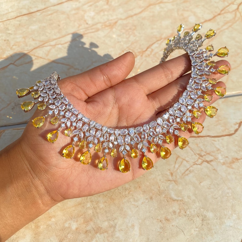 May include: A silver necklace with a row of clear cubic zirconia stones and a fringe of yellow teardrop-shaped stones.
