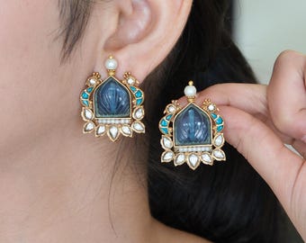 以下が含まれることがあります： アーチ型のフレームに中央の彫刻された青い石をあしらったゴールドトーンのイヤリング。ターコイズブルーのエナメル、小さな白い真珠、透明な涙型の石で装飾されています。上部の角には様式化された鳥のモチーフが施されています。