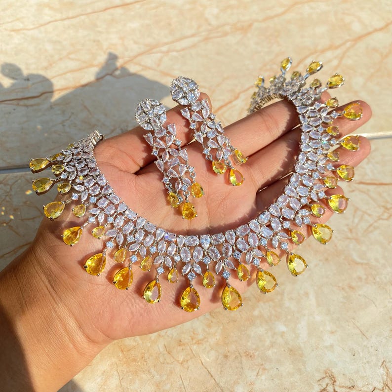 May include: A silver necklace and earrings set with clear and yellow teardrop-shaped stones. The necklace has a delicate design with a row of clear stones and a row of yellow stones.