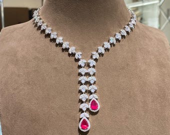 May include: A dazzling necklace featuring a floral design with clear stones and two teardrop-shaped, ruby-red pendants. The necklace is displayed on a brown mannequin, showcasing its intricate details and elegant style.