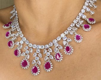 May include: A dazzling necklace featuring a silver-toned metal setting adorned with numerous clear, sparkling stones. The necklace is accented with vibrant, teardrop-shaped ruby-red gemstones, creating a luxurious and eye-catching design.