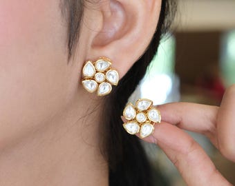 以下が含まれることがあります： 花柄のゴールドトーンのスタッドピアス。各ピアスは、中央の丸い白い石の周りに5つの涙型の白い石が円形に配置されており、磨かれたゴールドカラーの金属フレームにセットされています。