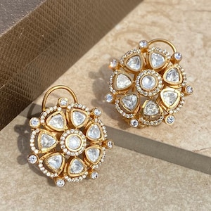 May include: A pair of gold earrings with a floral design. Each earring features a circular center stone surrounded by smaller stones in a triangular shape.