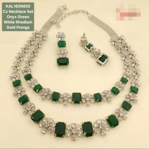 May include: A Cz necklace set with onyx green stones and white rhodium plating. The set includes a necklace and matching earrings. The necklace features a double-strand design with emerald-cut green stones and clear accents. The earrings have a similar design.