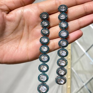 Pu&ograve; includere: Orecchini pendenti lunghi con una serie di pietre ovali trasparenti circondate da accenti color teal. Gli orecchini sono progettati con una disposizione lineare di pietre, creando un look sofisticato ed elegante. Un gioiello.
