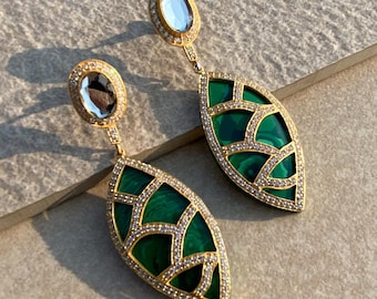 May include: A pair of gold-toned earrings with a leaf-shaped design. The earrings feature a green malachite inlay, surrounded by a border of small, clear crystals. The top of each earring has a blue-grey oval stone, also surrounded by crystals.
