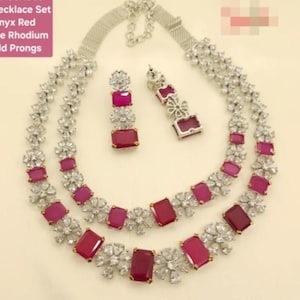 Peut inclure: Ensemble de bijoux argentés comprenant un collier à deux rangs et des boucles d'oreilles assorties. Les bijoux sont ornés de pierres claires et scintillantes et de pierres roses foncées rectangulaires. Le collier et les boucles d'oreilles ont un motif floral.
