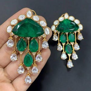 May include: A pair of gold earrings with a large green gemstone and smaller green and white gemstones hanging from the bottom.