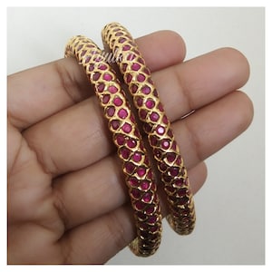 Pode incluir: Dois braceletes de ouro com um design de pedras cor-de-rosa. Os braceletes estão empilhados um em cima do outro.