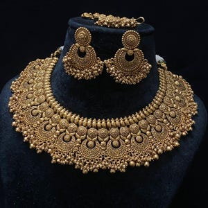 May include: A gold-tone necklace set with intricate floral and crescent moon designs. The necklace is thick and has a choker style. The earrings are dangle style with matching designs.