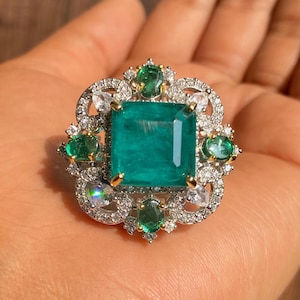 May include: A silver ring featuring a large emerald green gemstone surrounded by smaller emerald green and white gemstones.