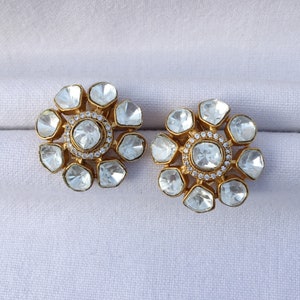 May include: A pair of gold earrings with a flower design. Each earring has a central round stone surrounded by smaller stones in a flower shape.