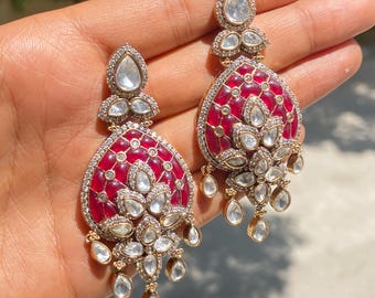 May include: A pair of ornate drop earrings featuring a large, teardrop-shaped central section with deep red, translucent enamel inlay. The gold-tone metal frame is encrusted with numerous small, clear, faceted stones and larger, pear-shaped clear stones.