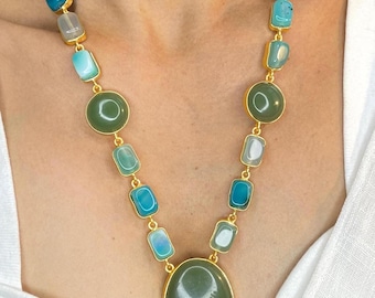 May include: A gold-toned necklace featuring a variety of green and blue gemstones. The necklace has an oval pendant and circular and rectangular stones. The gemstones are set in gold-colored metal, creating a striking contrast.
