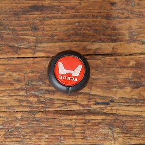 May include: A black gear shift knob with a red Honda logo and the word "HONDA" in white lettering.