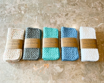 May include: Five knitted linen dishcloths in various colours, including white, grey, blue, and green. Each cloth has a brown label that reads "Linen Dish Cloths 100% cotton handmade reusable eco-friendly".