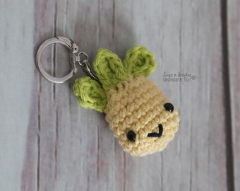 May include: A crocheted pineapple keychain with a smiling face, green leaves, and black eyes. The keychain is attached to a silver key ring.