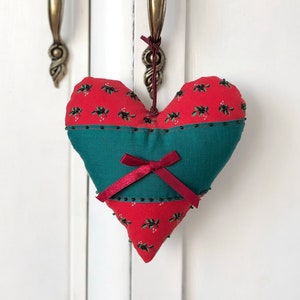 May include: A red and green heart-shaped pillow with a red bow hanging from a white door with gold handles.