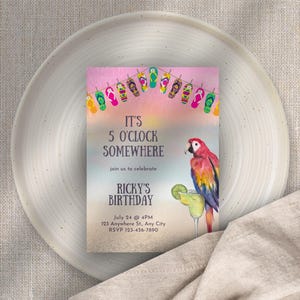 Puede incluir: Una tarjeta de invitación con temática tropical con el texto "IT'S 5 O'CLOCK SOMEWHERE" y "RICKY'S BIRTHDAY". La tarjeta presenta una ilustración de acuarela de un loro, margarita y chanclas. La invitación está sobre un plato blanco.