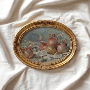 May include: An oval-shaped, gold-framed painting depicting several red onions on a light blue and white surface. The painting has a vintage aesthetic, with a detailed gold frame.