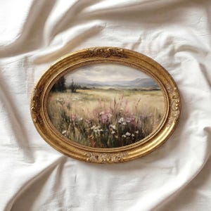 May include: An oval-shaped, gold-colored framed painting of a field of wildflowers. The artwork depicts a landscape with a variety of wildflowers in shades of pink, white, and yellow. The frame has an ornate, detailed design.