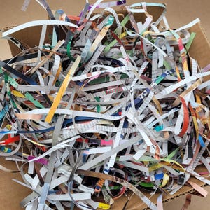 May include: A close-up of a cardboard box filled with colorful shredded paper. The paper is made from recycled materials and is perfect for packing fragile items.