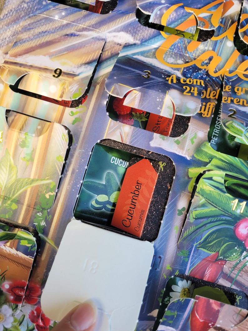 May include: An open advent calendar with several compartments visible. One compartment reveals a small packet labeled "Cucumber Cucumis" with an orange tag. Other compartments show images of plants and the numbers 2, 3, 9, 11, and 18.