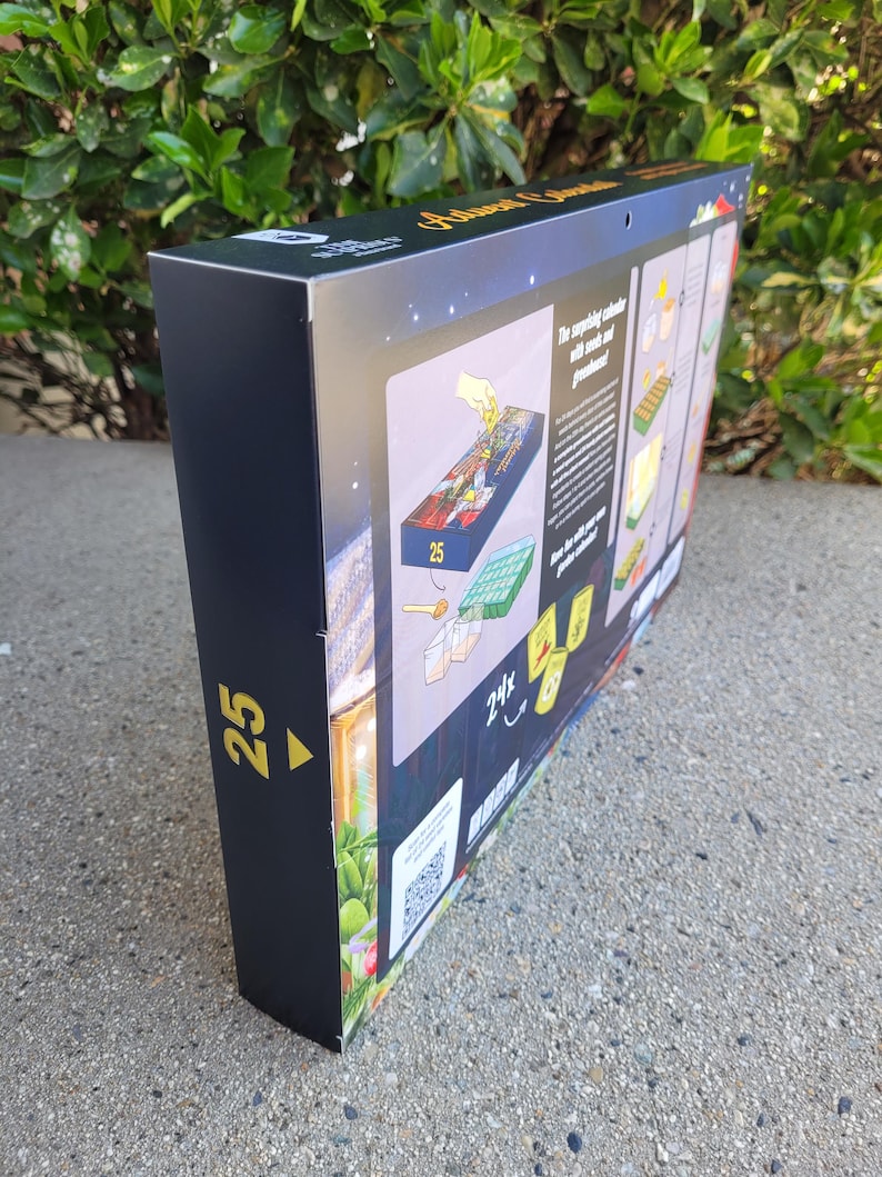 May include: A black box with gold text and illustrations. The box is for an Advent calendar, with the number 25 in gold on the side. The box has a QR code and images of the calendar's contents.