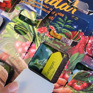 May include: An Advent calendar with open windows revealing seed packets. The calendar has a dark blue background with gold lettering. One window is open, displaying a yellow label that reads "Tarragon Artemisia". Other windows show illustrations of vegetables.