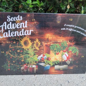 May include: Seeds Advent Calendar with a Christmas tree, sunflowers, and tomato plants. The calendar has 24 numbered windows and the text "A complete growhouse set with 24 different seed sachets."