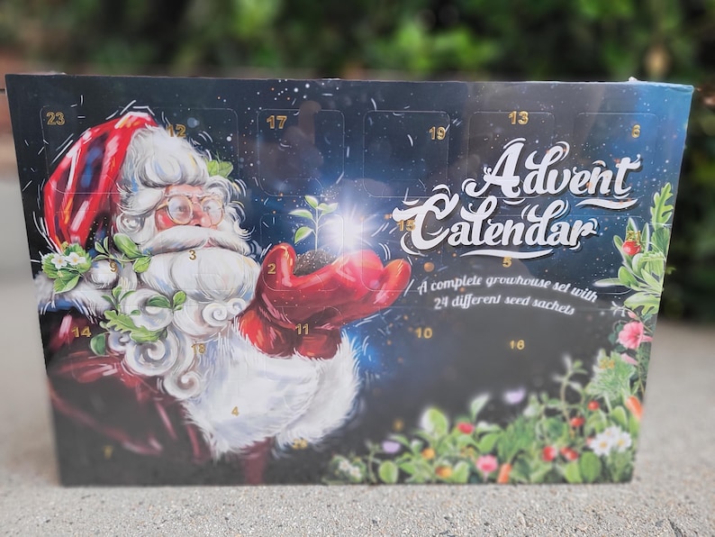 May include: Advent calendar featuring Santa Claus holding a sprouting plant. The calendar has a dark blue background with the words "Advent Calendar" in white script. It includes 24 seed packets for a complete greenhouse set.