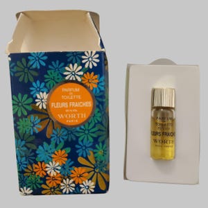 May include: A vintage perfume set featuring a small glass vial and a decorative box. The box is navy blue with a floral pattern in white, orange, and teal. The vial contains a yellow liquid and is labeled "FLEURS FRAICHES" by WORTH, PARIS.