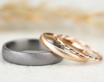 May include: Three wedding bands, one is a brushed silver band, one is a brushed rose gold band, and the third is a twisted rose gold band.