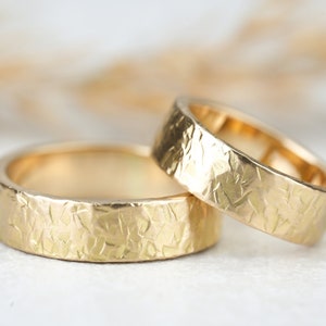 Op de afbeelding: Twee gouden trouwringen met een getextureerde, gehamerde afwerking. De ringen zijn op elkaar gestapeld.