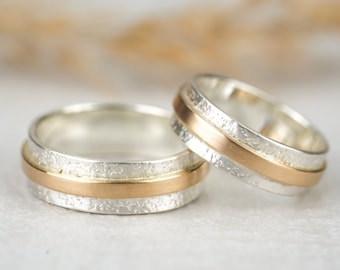 May include: Two wedding bands, one silver with a gold band, the other gold with a silver band.