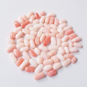 May include: A collection of oval-shaped gemstones in varying shades of pink and white. The gemstones are smooth and polished, with a glossy appearance. The arrangement is scattered, creating a visually appealing display of natural beauty. The gemstones are likely used for jewelry making.