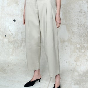 May include: A pair of light beige wide-leg pants with pleats. The pants are made of a lightweight fabric and have a relaxed fit.