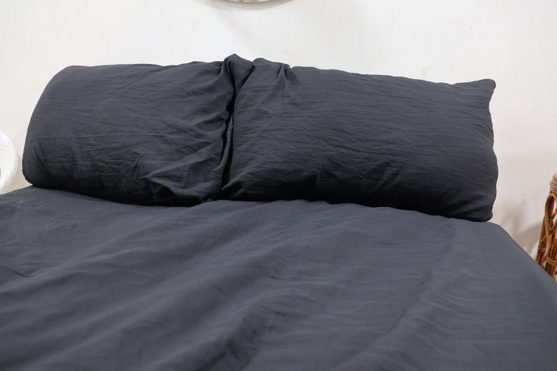 May include: A dark charcoal gray bedding set consisting of a duvet cover and two matching rectangular pillows. The fabric has a soft, slightly wrinkled texture and a matte finish, covering the entire surface of the bed in a uniform dark tone.