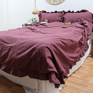 May include: A burgundy ruffled duvet cover with white ruffles around the edges. The duvet cover is on a bed with white sheets and pillows.