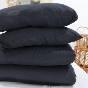 May include: A stack of four rectangular pillows and bedding items in a solid dark charcoal black color. The items are layered horizontally on top of each other, featuring a soft, matte fabric texture with visible seams along the edges of each piece.
