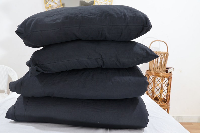 May include: A stack of four rectangular pillows and bedding items in a solid dark charcoal black color. The items are layered horizontally on top of each other, featuring a soft, matte fabric texture with visible seams along the edges of each piece.